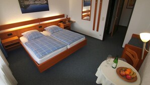 Una habitación de hotel con una cama doble, una mesita con frutero y una botella de vino.