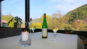 Una mesa con una vela, una botella de vino y dos copas de vino, con vistas a una colina y árboles.
