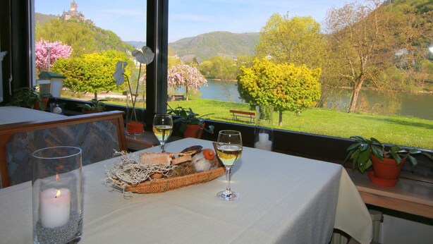 Una mesa con una vela, copas de vino y una cesta de pan, con vista a un paisaje panorámico de un lago y árboles.