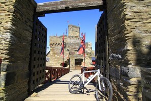A wooden bridge leading to a stone castle with flags, a bicycle, and a wooden fence. - Hotel Weinstube Klasen (Cochem)