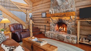 L’intérieur d’une cabane en rondins, avec une cheminée en pierre, un fauteuil en cuir et un escalier.