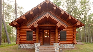 Une cabane en rondins avec des fondations en pierre, une porte d’entrée en bois et une véranda avec des marches menant à l’entrée.