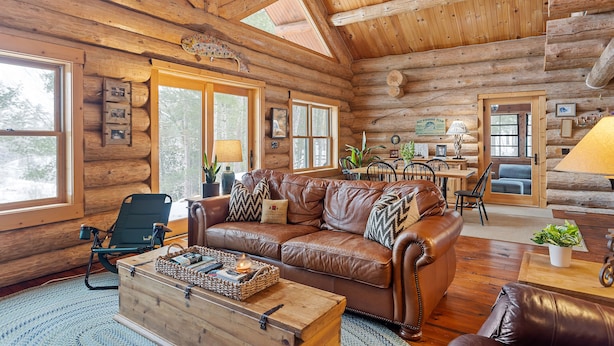 L’intérieur d’une cabane en rondins, avec un canapé en cuir, une table basse en bois et de grandes fenêtres.