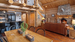 L’intérieur d’un chalet rustique en rondins de bois, avec une cheminée en pierre, une table à manger en bois et un coin salon confortable.