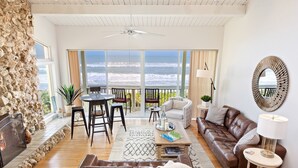 A spacious living room with a stone wall, a fireplace, a leather sofa, a coffee table, and a view of the ocean through large windows. - Oceanfront 3-Bedroom / 2-Bath Luxury Townhouse in the heart of Melbourne Beach (Melbourne Beach)