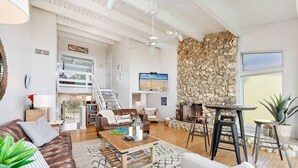 A spacious living area with a high ceiling, a stone wall, a wooden coffee table, leather sofas, and a TV mounted on the wall. - Oceanfront 3-Bedroom / 2-Bath Luxury Townhouse in the heart of Melbourne Beach (Melbourne Beach)