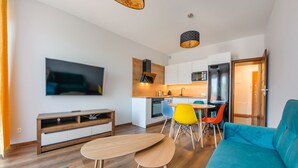 A modern living room with a flat-screen TV, a wooden coffee table, a teal sofa, and a dining area with a small table and colorful chairs. - Apartamenty Sun & Snow Ustka Aquarius (Ustka)