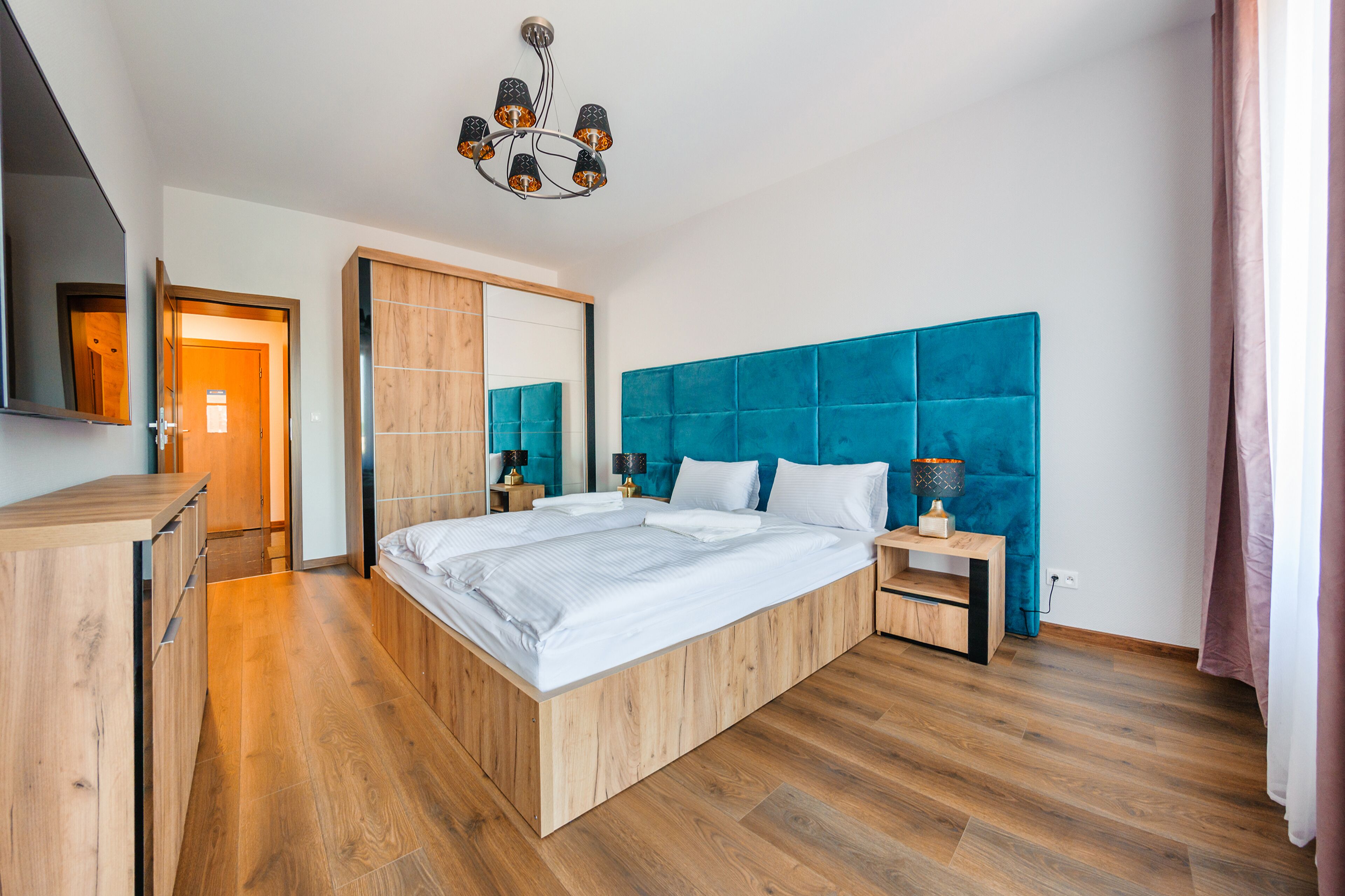Un dormitorio moderno con una cama de madera, un espejo grande, un cabecero azul y un aparador de madera.