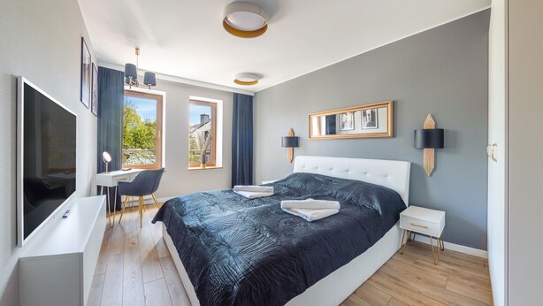 A modern bedroom with a large bed, a desk, and a chair. - Apartamenty Sun & Snow Ustka Aquarius (Ustka)