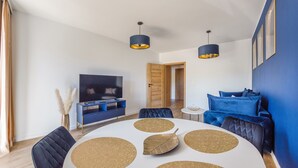 A modern living room with a round dining table, blue sofa, and a TV on a wooden cabinet. - Apartamenty Sun & Snow Ustka Aquarius (Ustka)