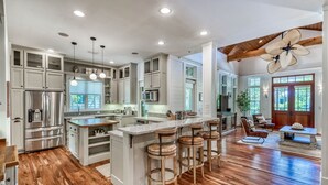 A spacious kitchen with wooden floors, white cabinetry, and a large island with bar stools.