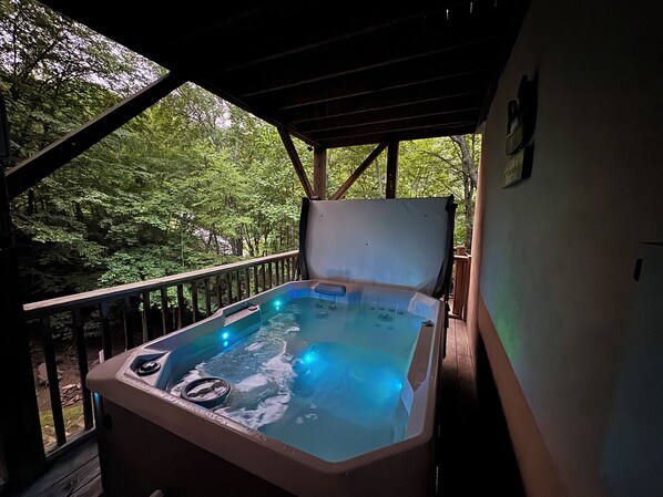 A hot tub on a wooden deck with a view of a forest. - 3BR_3BA Log Cabin, Pond Front, Hot Tub, Pool Table, near Skiing & Pet friendly (Seven Devils)