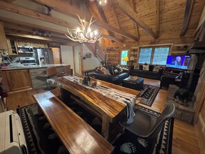 A rustic interior with a wooden dining table, a kitchen with modern appliances, a living area with a television, and a fireplace. - 3BR_3BA Log Cabin, Pond Front, Hot Tub, Pool Table, near Skiing & Pet friendly (Seven Devils)