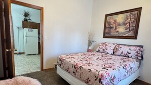 A bedroom with a bed, a ceiling fan, a painting, and a door leading to another room.