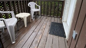 A wooden deck with a black metal railing, two white plastic chairs, and a small table.