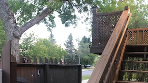A wooden deck with a metal railing, a barbecue grill, and a paved pathway leading to a fence.