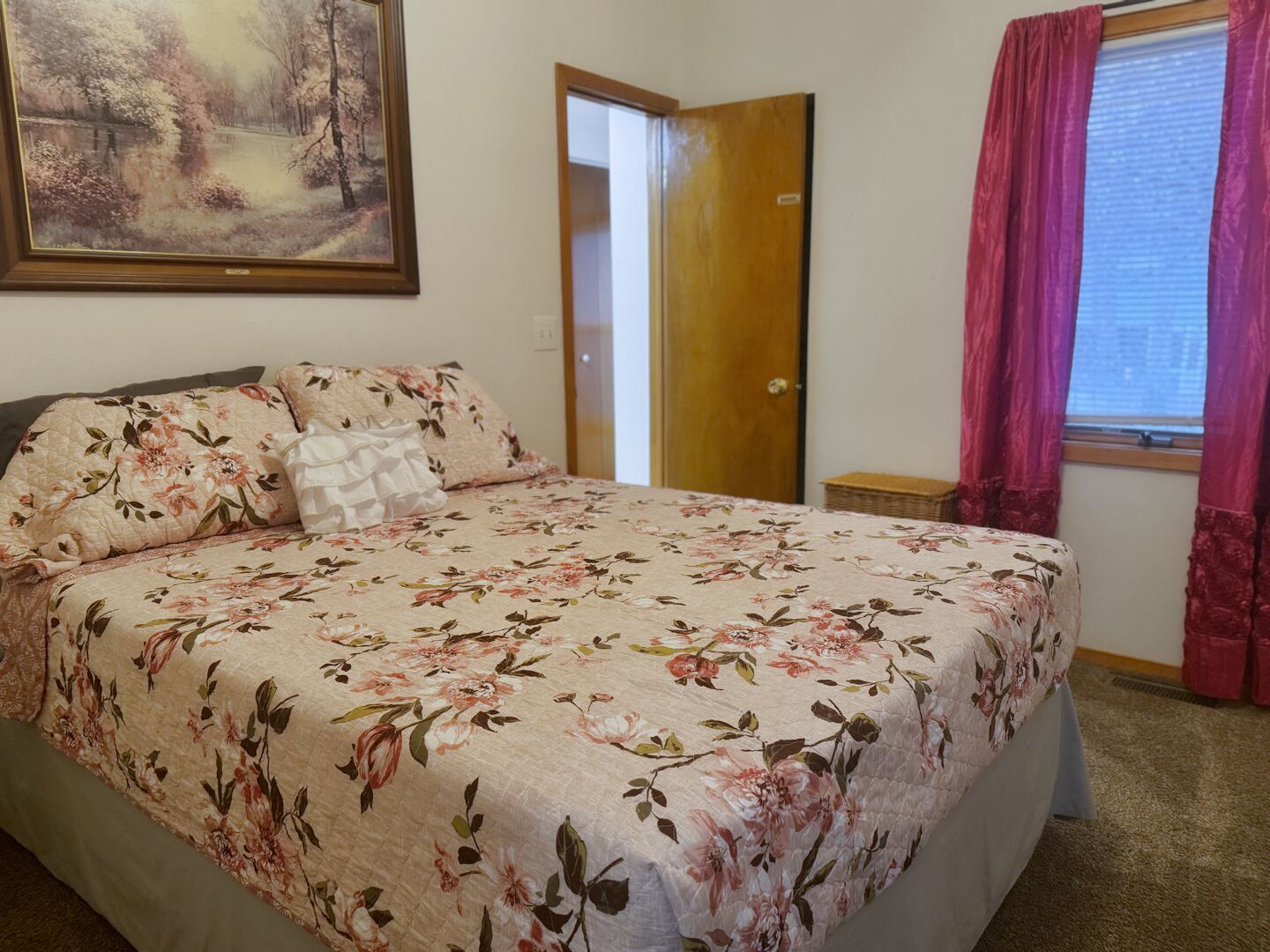 Ein Schlafzimmer mit Blumenmuster-Bettdecke, einem Bild an der Wand und einem Fenster mit Vorhängen.