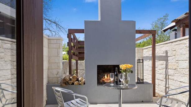 Une terrasse extérieure avec un mur en pierre, une table en métal, deux chaises, un foyer et une pergola en bois.
