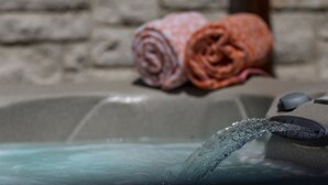 Une baignoire remplie d’eau, un mur en pierre et deux serviettes enroulées.