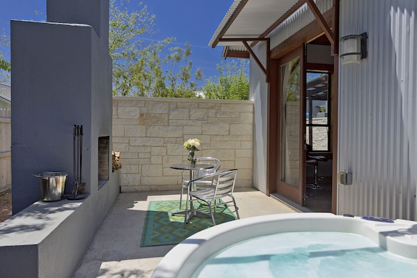 A patio with a hot tub, stone wall, metal chairs, and a small table with a vase of flowers.