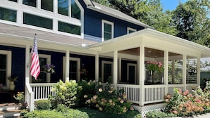 A two-story house with a covered porch, a flag, and various potted plants. - Beautiful new large family home inside gates of Country Club of Sapphire Valley. (Sapphire)