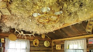 Une chambre rustique dans un chalet, avec un lit, des rideaux à carreaux, une tête de lit en bois, un lustre et une horloge murale.