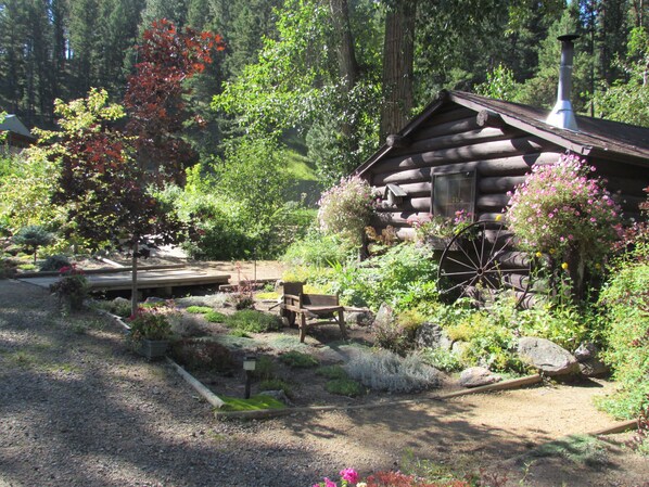 A rustic log cabin surrounded by a well-maintained garden with a wooden bench and a large wheelbarrow. - Tizer Botanic Gardens Cabin 1/2 way between Yellowstone & Glacier National Parks (Jefferson City)