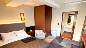 A hotel room with a large bed, a desk, a chair, and a bathroom visible through an open door. - PLACE Hotel Ascot (Kumamoto)