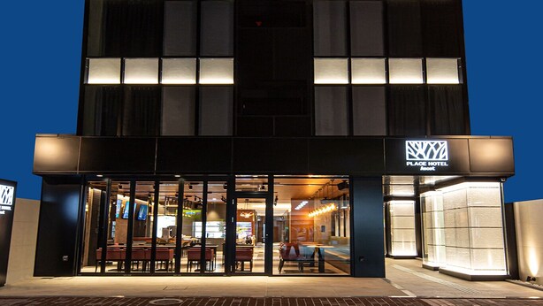 A modern hotel with a symmetrical facade, large windows, and a well-lit entrance. - PLACE Hotel Ascot (Kumamoto)