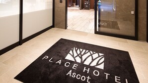 A hotel entrance with a black doormat reading "PLACE HOTEL Ascot" and a glass door leading inside. - PLACE Hotel Ascot (Kumamoto)