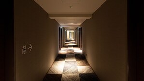 A hotel hallway with a checkered floor pattern, directional signs, and a ceiling light fixture. - PLACE Hotel Ascot (Kumamoto)