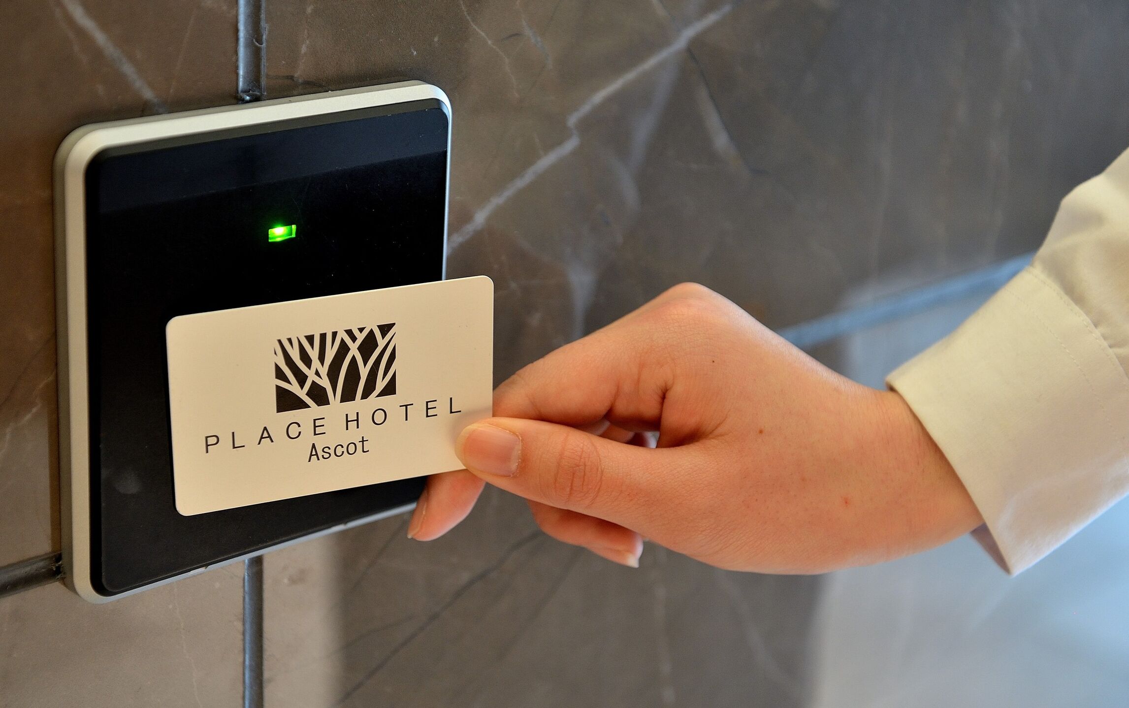 A hand holding a card with the logo and name "PLACE HOTEL Ascot" in front of a digital lock.