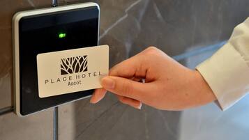 A hand holding a card with the logo and name "PLACE HOTEL Ascot" in front of a digital lock.
