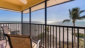 Een overdekt balkon met uitzicht op het strand, inclusief palmbomen en de oceaan.