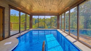Ein Hallenbad mit großen Glaswänden, einer Holzbalkendecke und Blick auf eine grüne Landschaft.