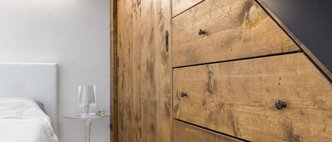 A bedroom with a bed, wooden wardrobe, and a small table with a lamp.
