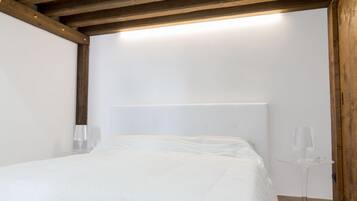 Une chambre avec un plafond en bois, un lit doté d’une tête de lit blanche et une petite table avec un plateau en verre.
