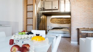 A room with a brick wall, a wooden staircase, a bed, and a table with fruits and a glass of wine. - Residence Le Bugne (Noale)