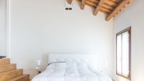 A modern bedroom with a large bed, wooden staircase, and a large window. - Residence Le Bugne (Noale)