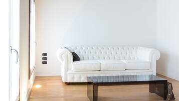 Un sofá blanco con respaldo capitonado y una mesa de centro negra en una habitación con suelo de madera y pared blanca.