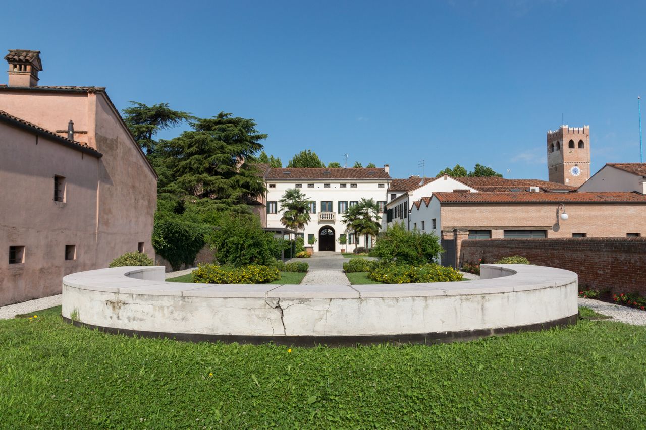 A courtyard with a central pathway leading to a building with a white facade and a tower.