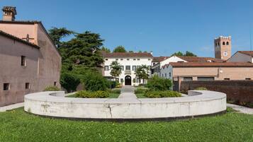 A courtyard with a central pathway leading to a building with a white facade and a tower.
