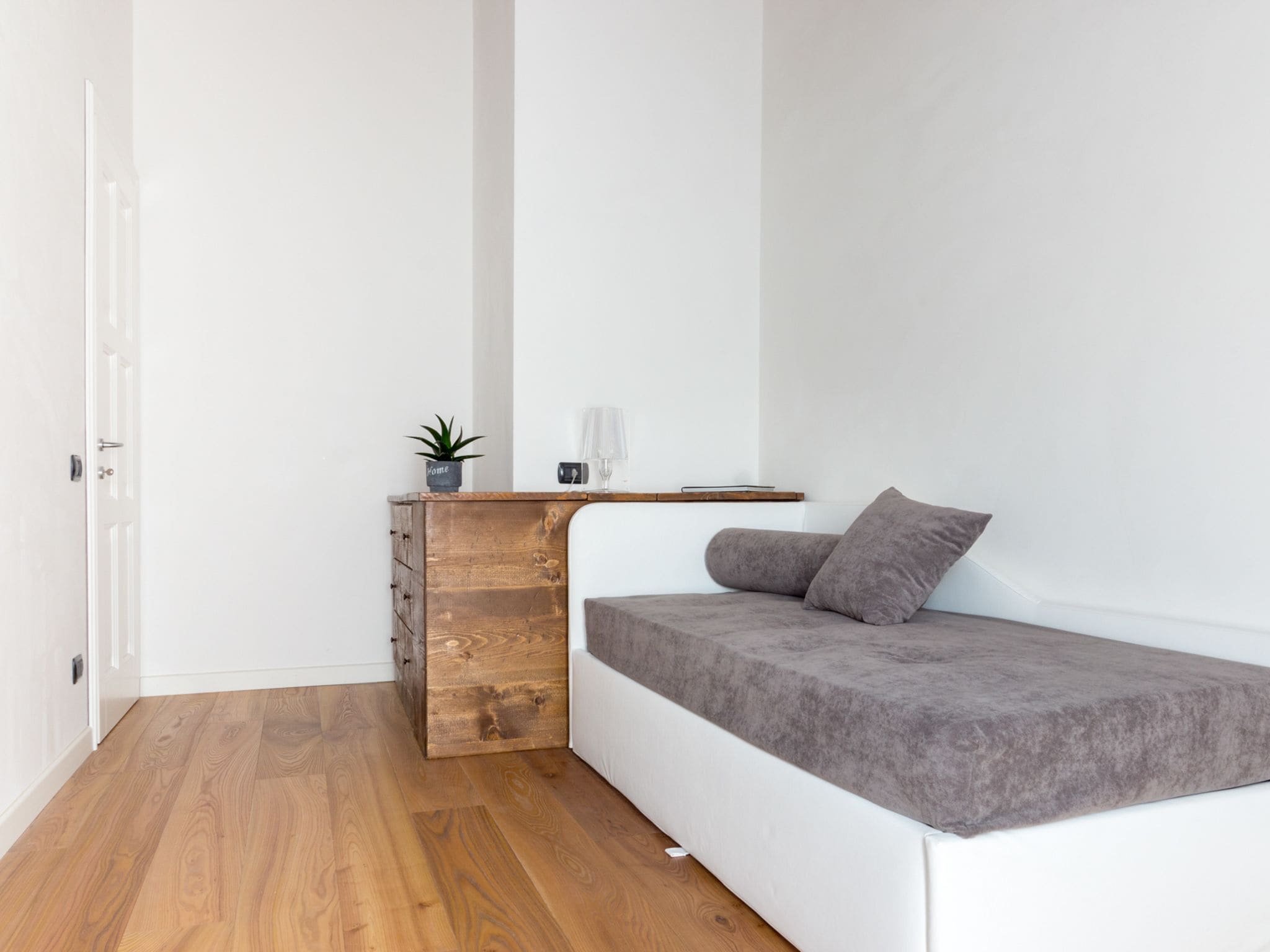 A compact room with a built-in sofa bed, a small wooden cabinet, and a potted plant.