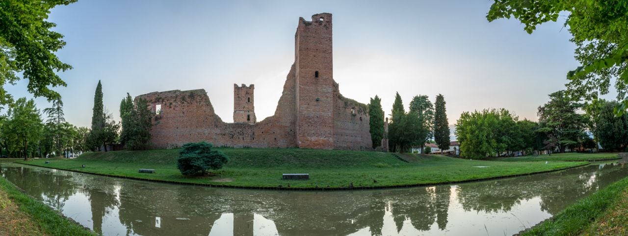 A historic brick castle with a moat, surrounded by trees and a grassy area.