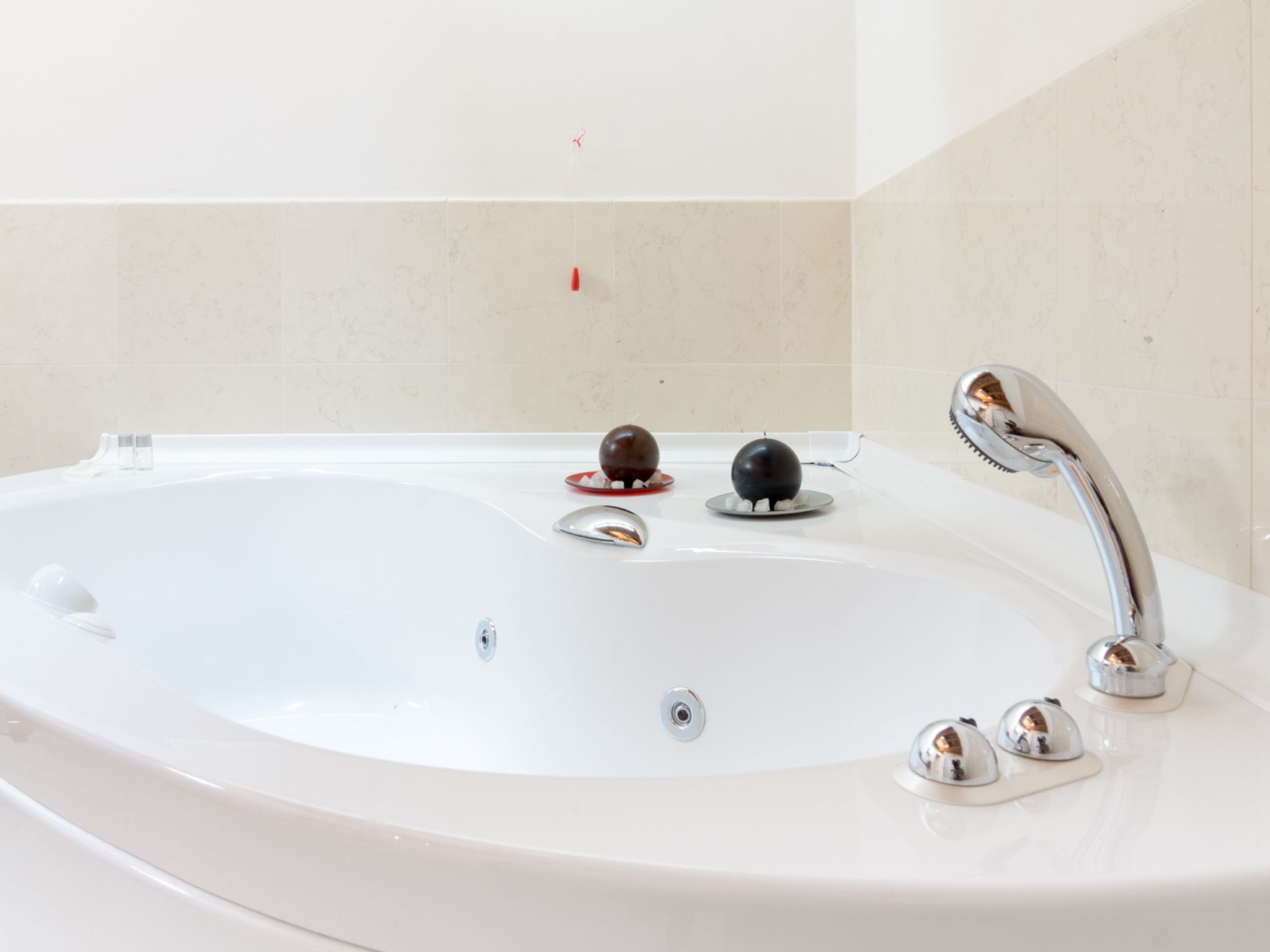 Eine weiße Badewanne mit einem chromfarbenen Wasserhahn und zwei kugelförmigen Objekten am Rand.