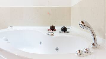 Eine weiße Badewanne mit einem chromfarbenen Wasserhahn und zwei kugelförmigen Objekten am Rand.