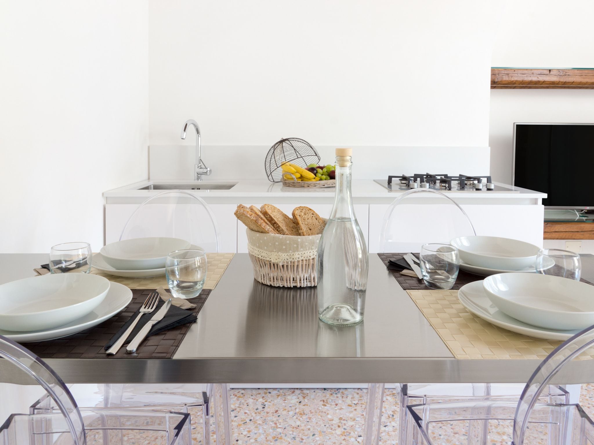 A modern kitchen with a dining table set for four, including plates, glasses, and cutlery.