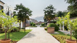 A pathway leading to a residential area with houses, palm trees, and a brick wall. - Residence Le Bugne (Noale)