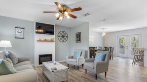 Un salon spacieux doté d’un ventilateur de plafond, d’une cheminée et d’un coin repas avec une table et des chaises.
