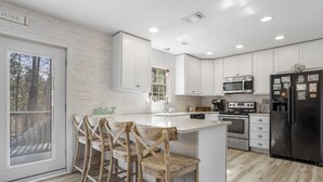 Une cuisine moderne avec des meubles blancs, un îlot central doté de tabourets, des appareils en acier inoxydable et une grande fenêtre.
